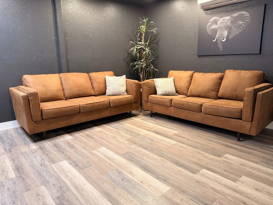 The client lounge at One Refined Heritage, with 2 camel leather sofas against a dark wall