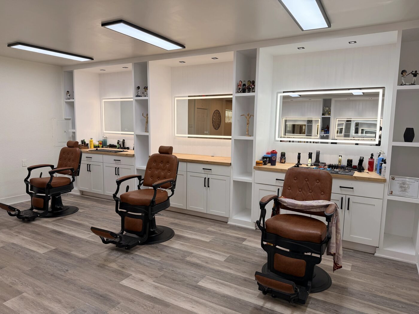 Camel leather barber chairs beside illuminated mirrors inside One Refined Heritage